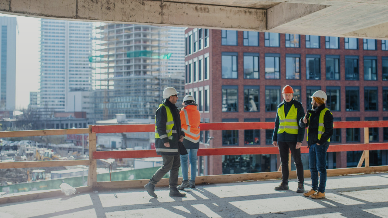 Four workers on a city scraper construction site in hi-vis and helmets.